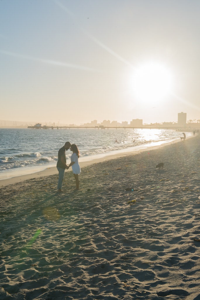 A young couple holds hands and touches foreheads on the beach one late afternoon.