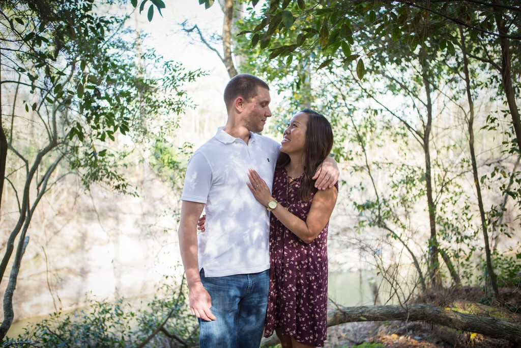 A Young couple embraces one another in the middle of a forest area on a sunny day.