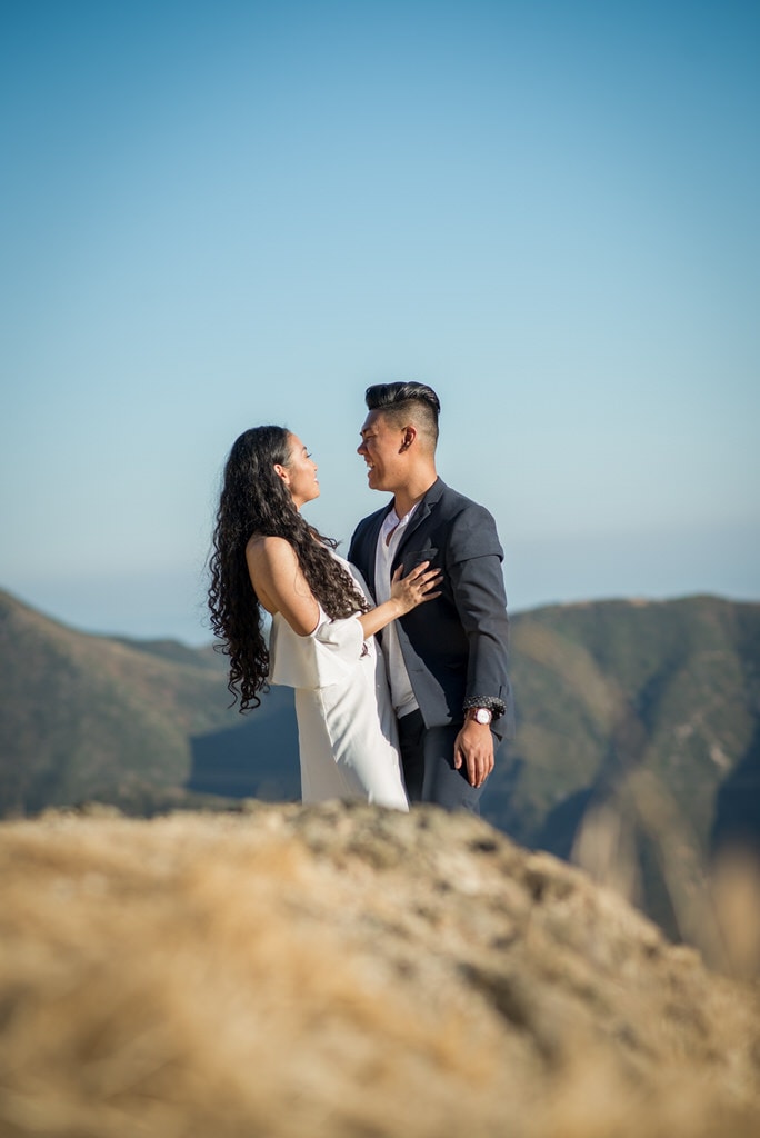 The photographer captures a gorgeous candid shot of a young newly engaged couple laughing and smiling at one another on a sunny day in the mountains of California.