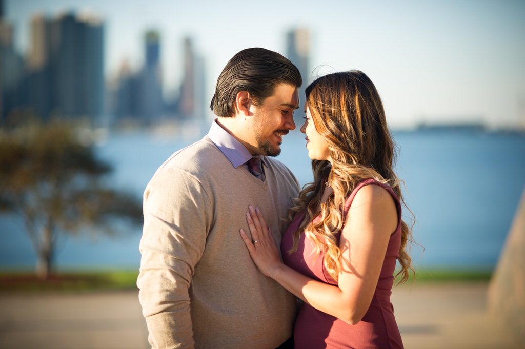 A newly engaged couple looks lovingly at one another as the sun sets on the city.