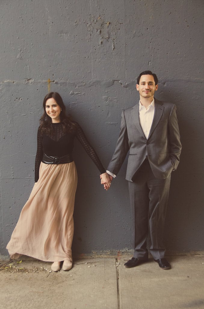 This couple stands against a slate grey wall holding hands ever so slightly yet so tightly that their love can be shown with one small gesture. Smiling away their love and all desires of happiness.