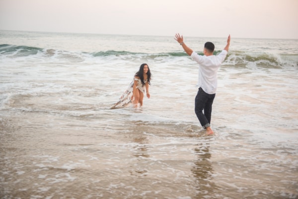The couple is walking through the water at the beach.