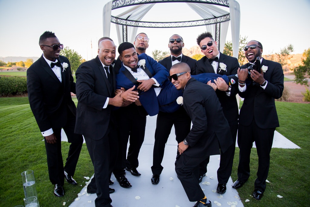 The charismatic groomsmen playfully lift the groom in the air while laughing and smiling for the wedding photographer. Beautiful iron gazebo rests behind them as the sun sets.