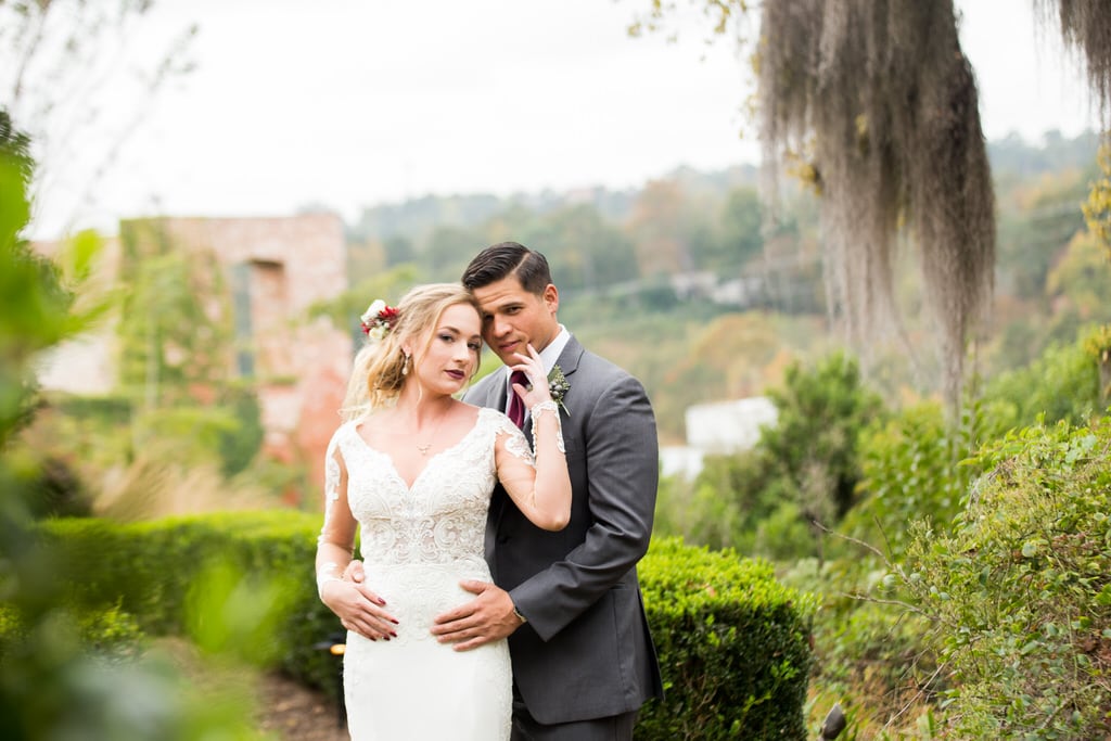 Bride and Groom give the photographer a sultry glance while in the garden. Greenery and old Willow trees rest in the background complimenting the Bride's floral hairpiece with deep red accents.