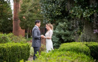 Candid photography of a Bride and Groom holding hands and exchanging words in the garden. Bushes, trees, and wildflowers surround them as they share a private moment.