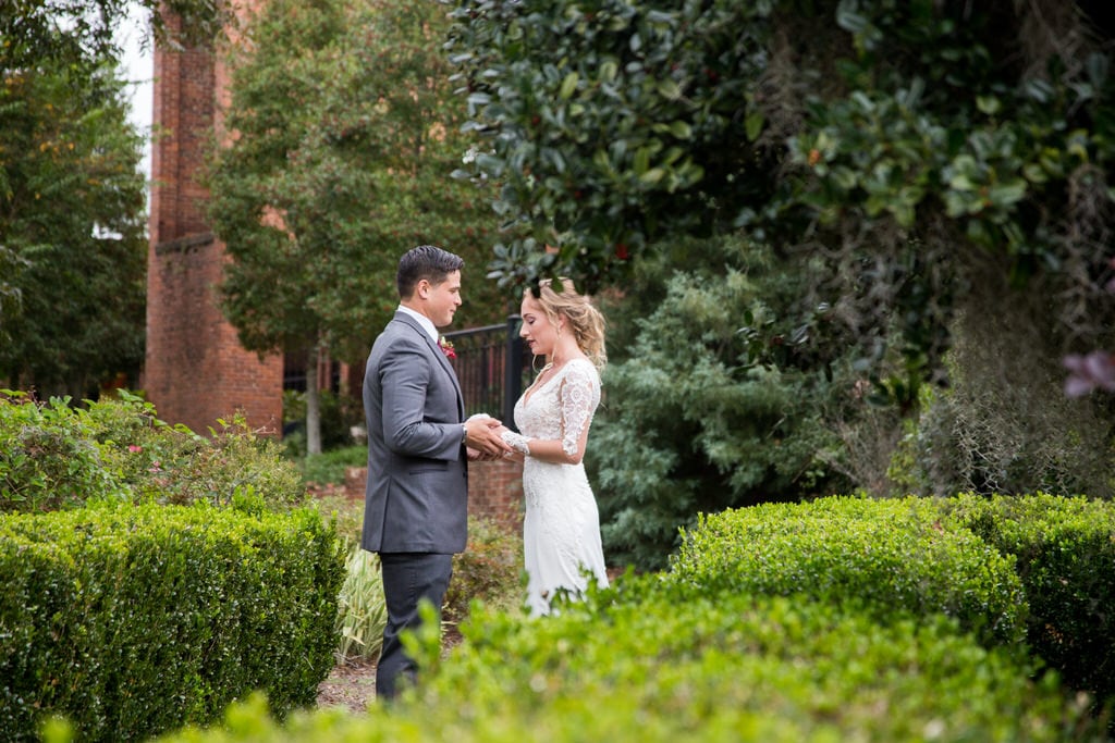 Candid photography of a Bride and Groom holding hands and exchanging words in the garden. Bushes, trees, and wildflowers surround them as they share a private moment.