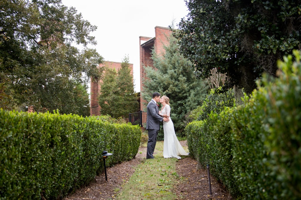 Newlywed Bride and Groom share a kiss at the entryway of a garden.