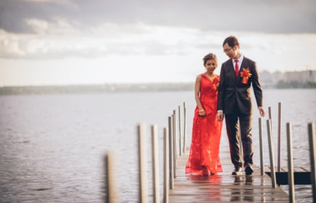 man in black suit and woman in red dress standing on sea dock during daytime