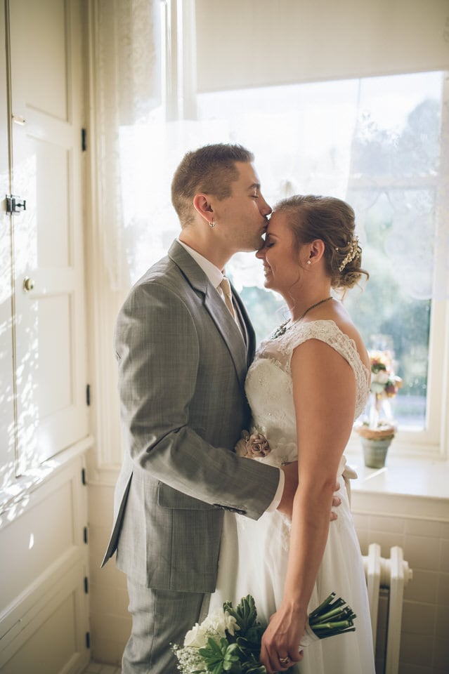 man in gray suit jacket kissing woman in white wedding dress