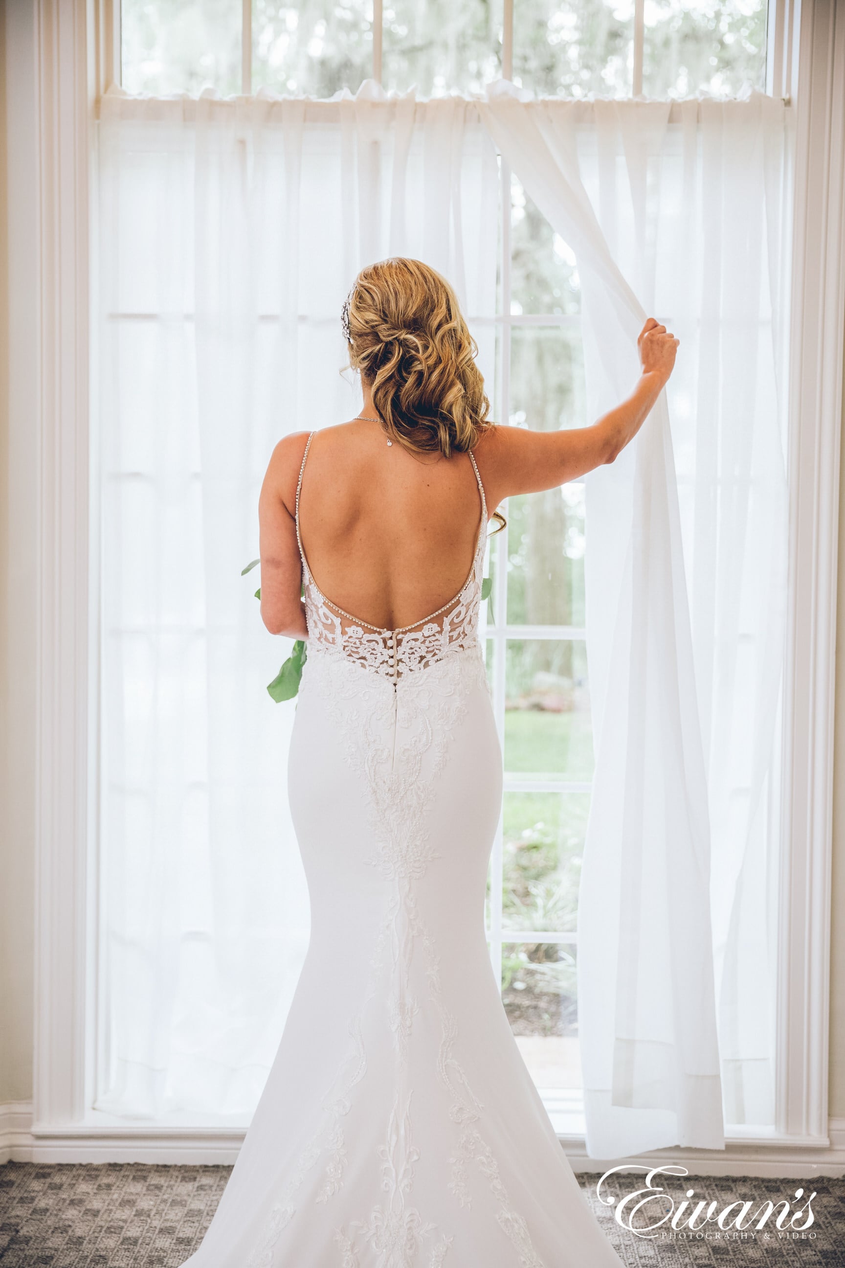 woman in white floral spaghetti strap dress standing near white window curtain