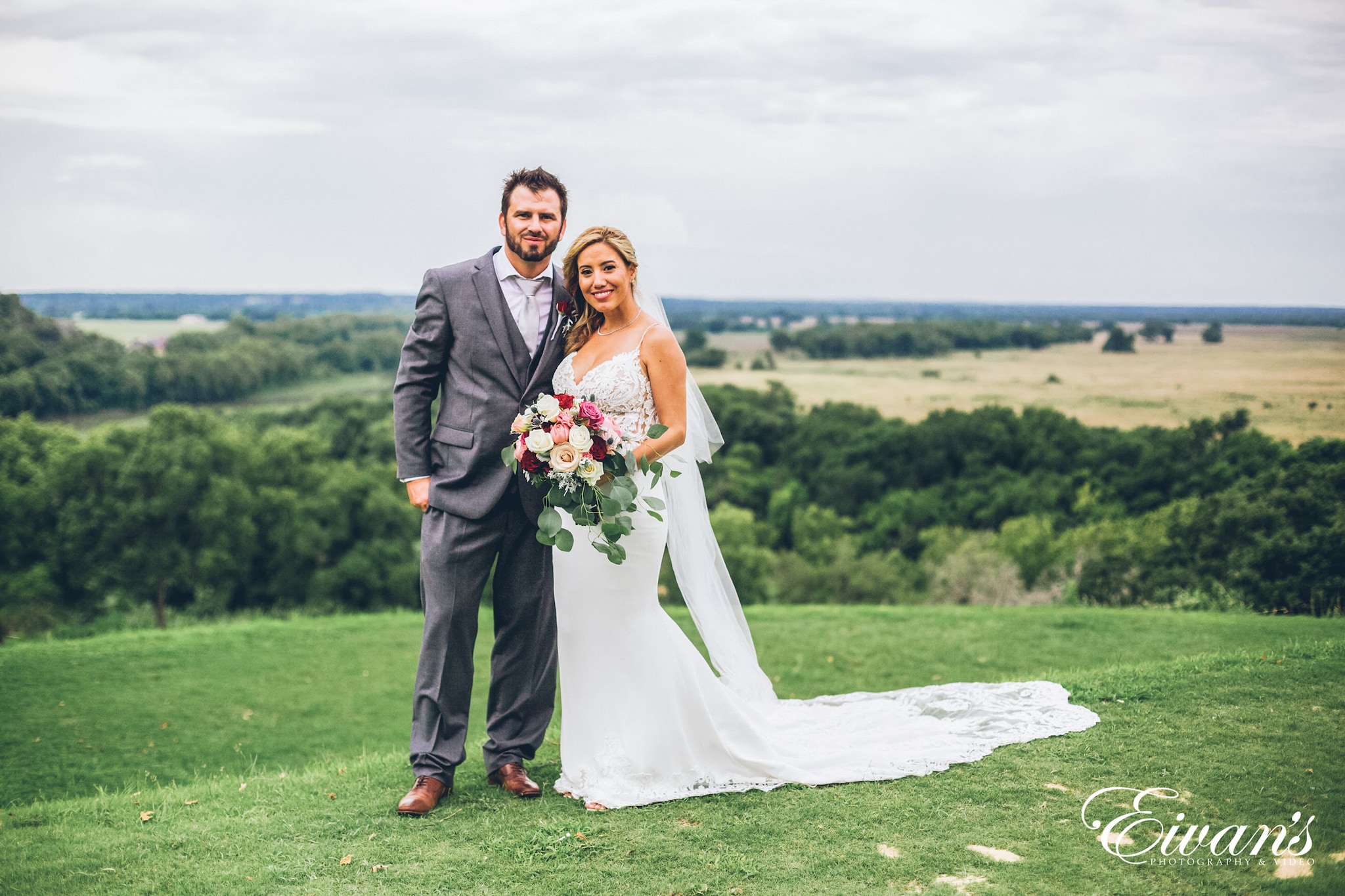 man in black suit and woman in white wedding dress holding bouquet standing on green grass