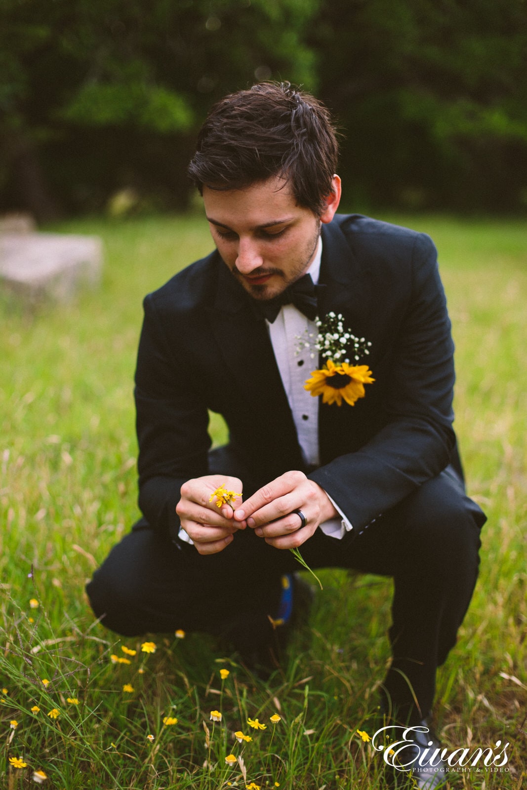 man in a black suit in a field of grass and yellow flowers