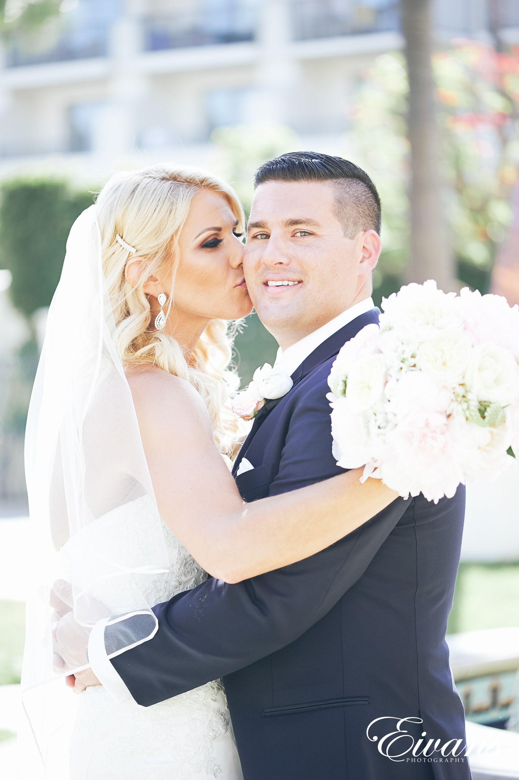 man in black suit kissing woman in white wedding dress