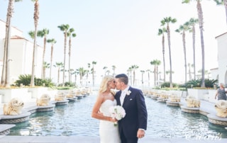 man in black suit kissing woman in white wedding dress near body of water during daytime