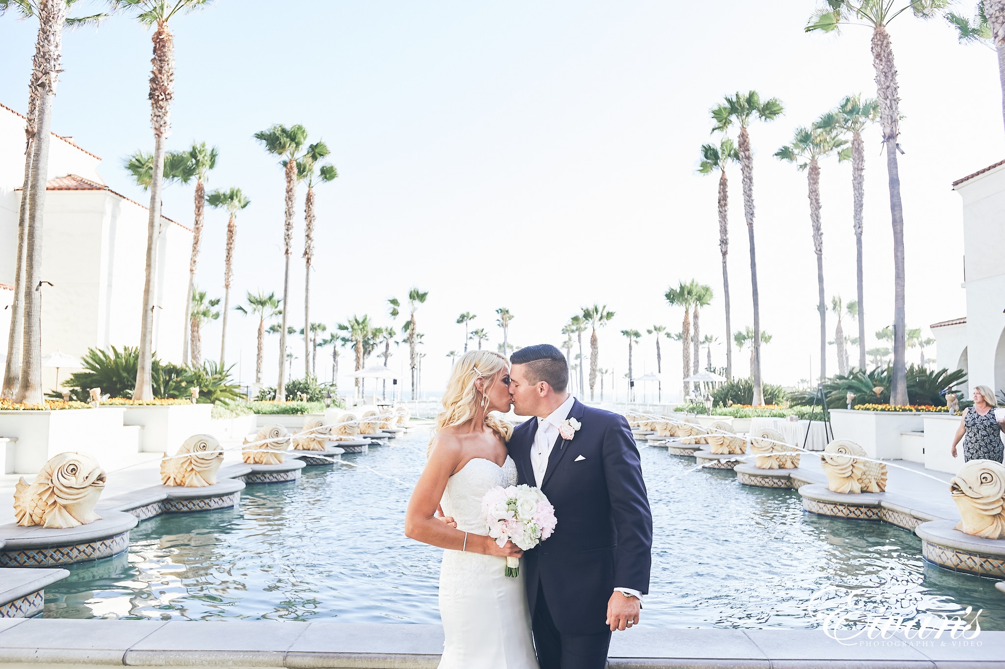 man in black suit kissing woman in white wedding dress near body of water during daytime