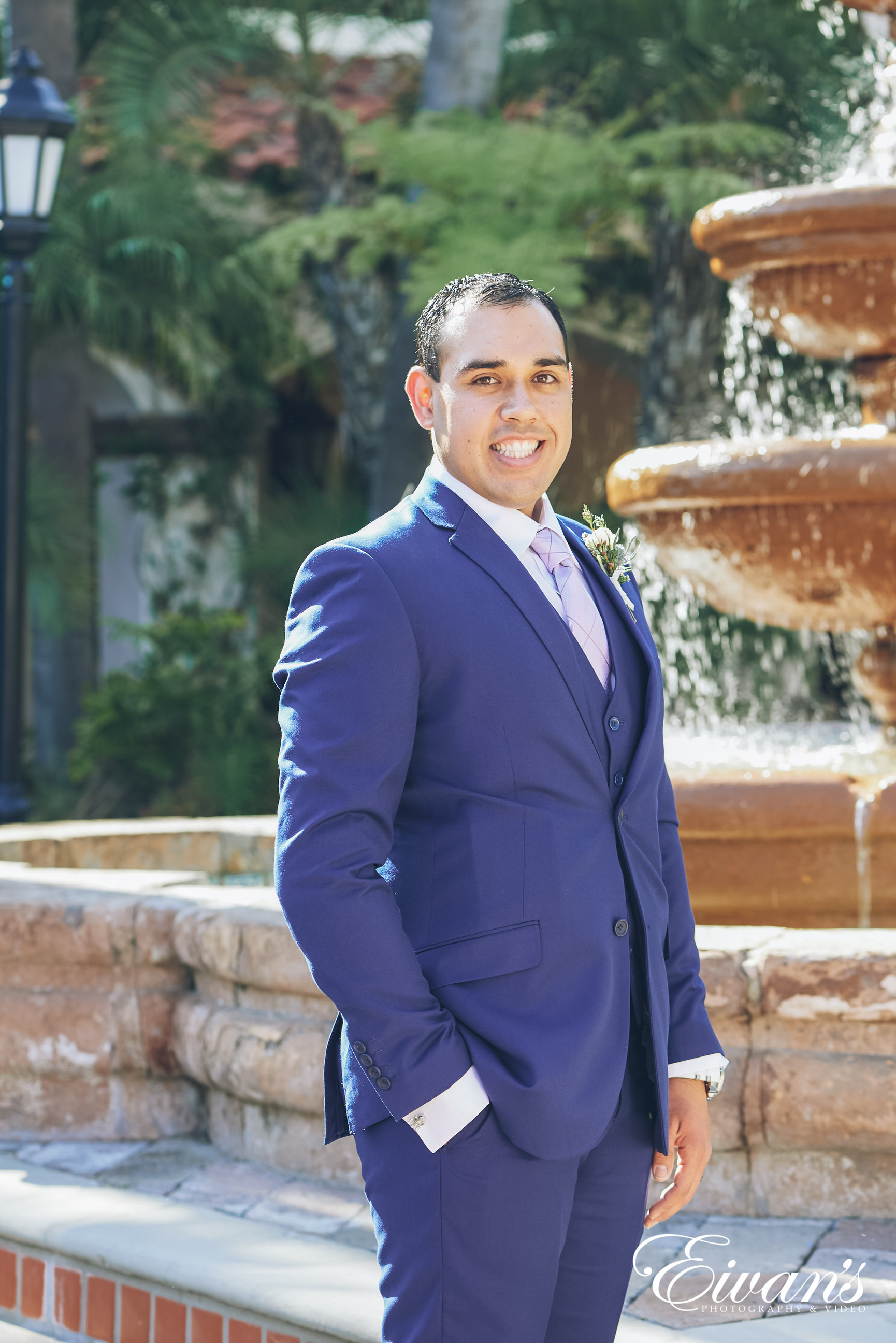 man wearing a dark blue suit posed in front of a fountain