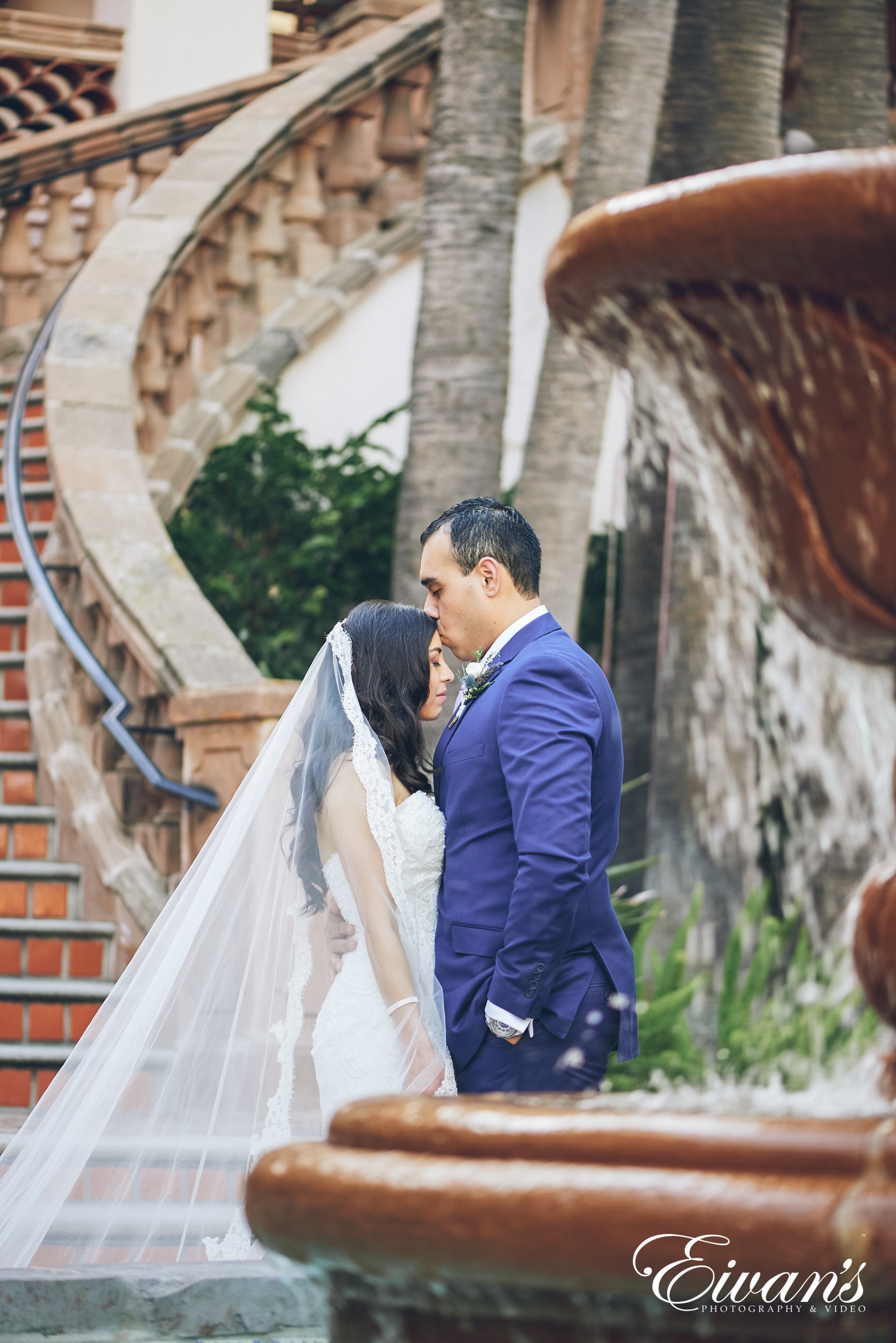 man kissing woman in a white dress on the forehead