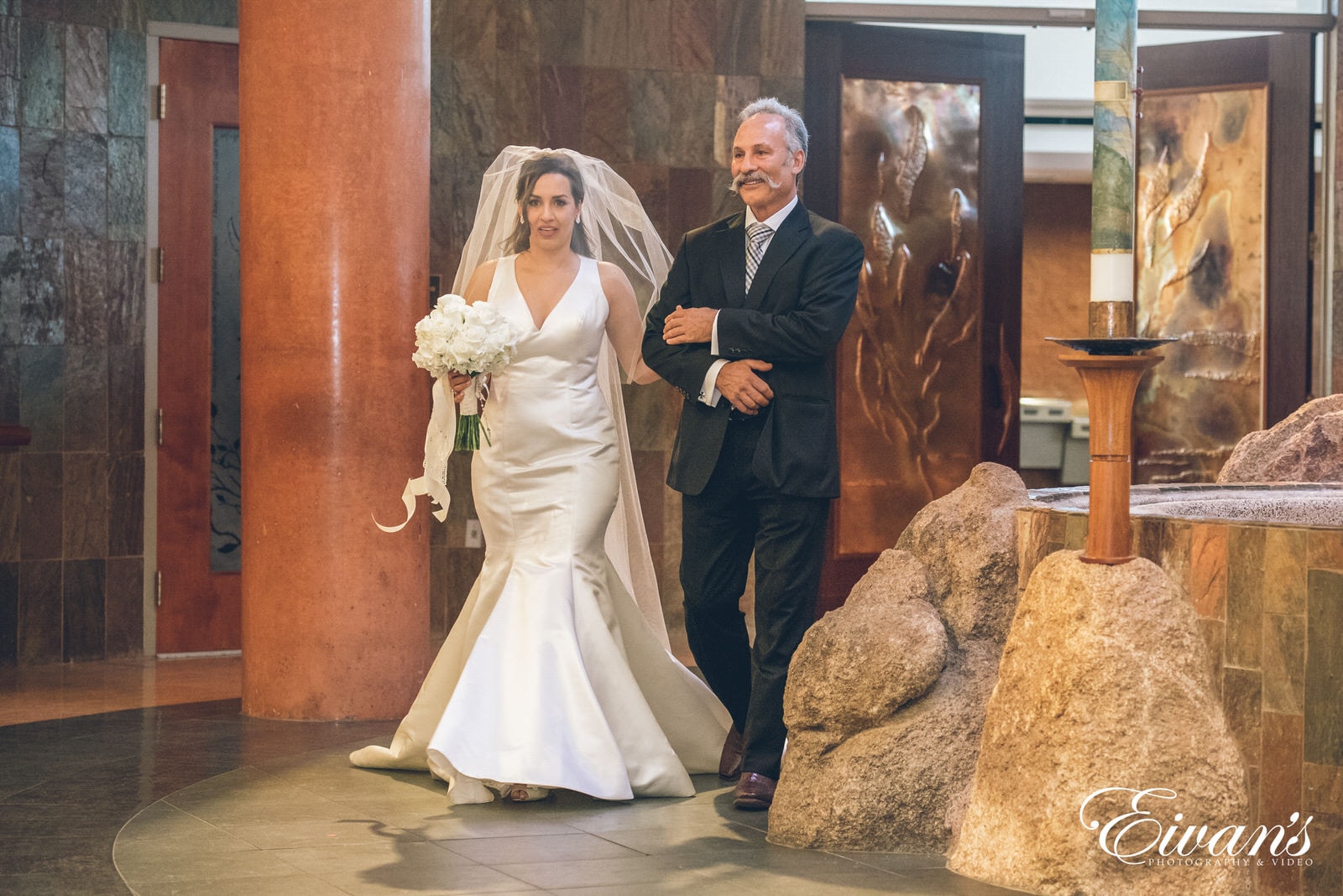 woman in a white dressing walking side by side next to a man in a suit