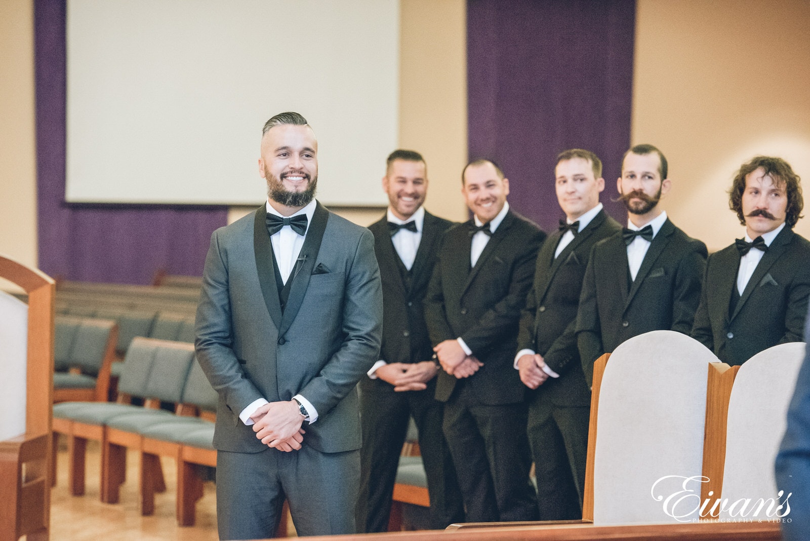 man in a dark grey suit standing next to five other men in black suits