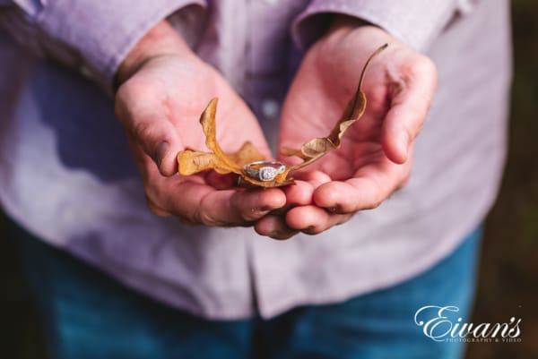 man holding ring in hands on top of a handful of autumn leaves