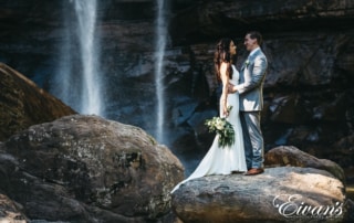 man and woman standing on rock near waterfalls during daytime