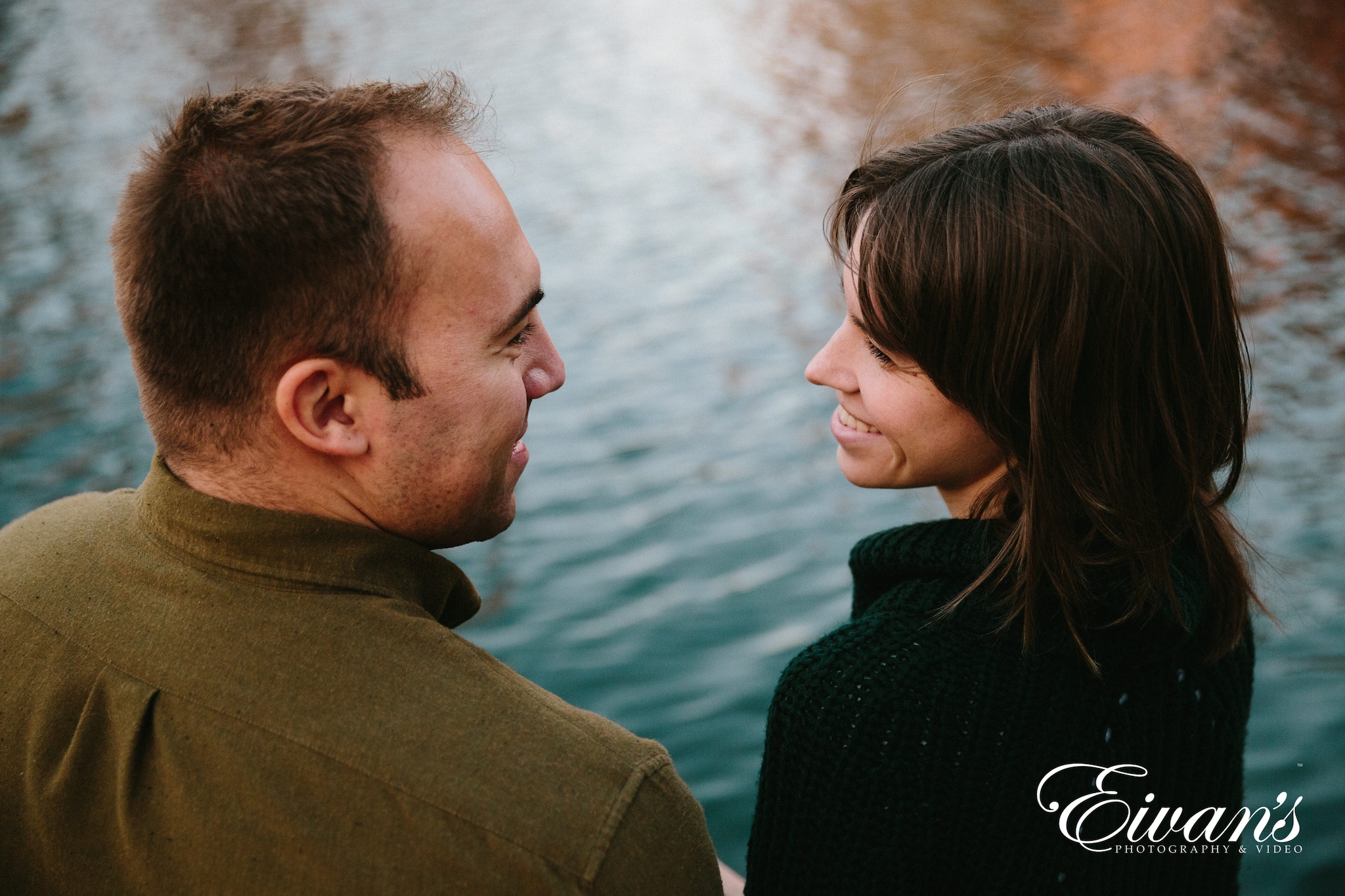 two engaged couple looking at each other in front of a lake