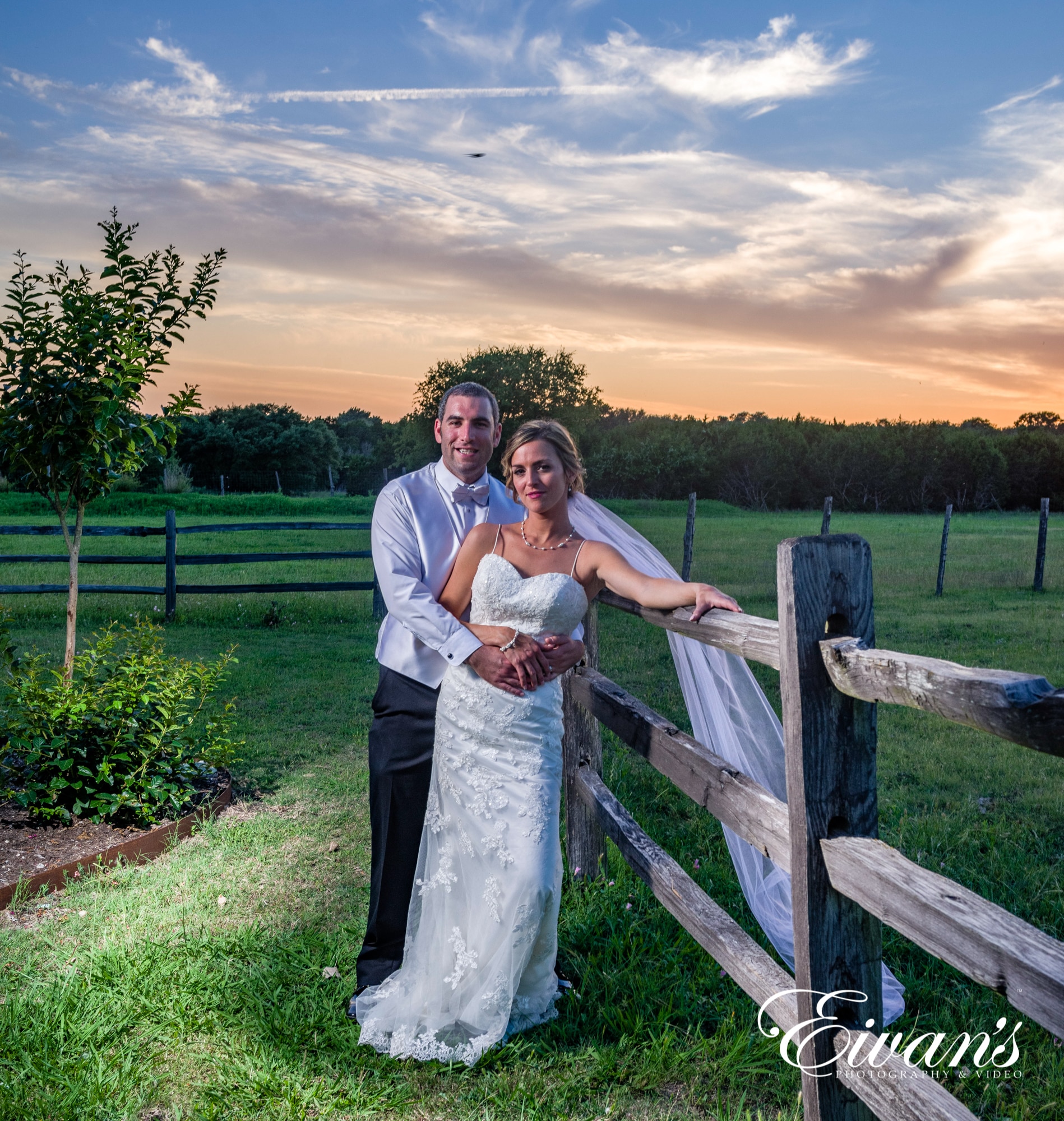 married couple posed on the barn fence in the sun set
