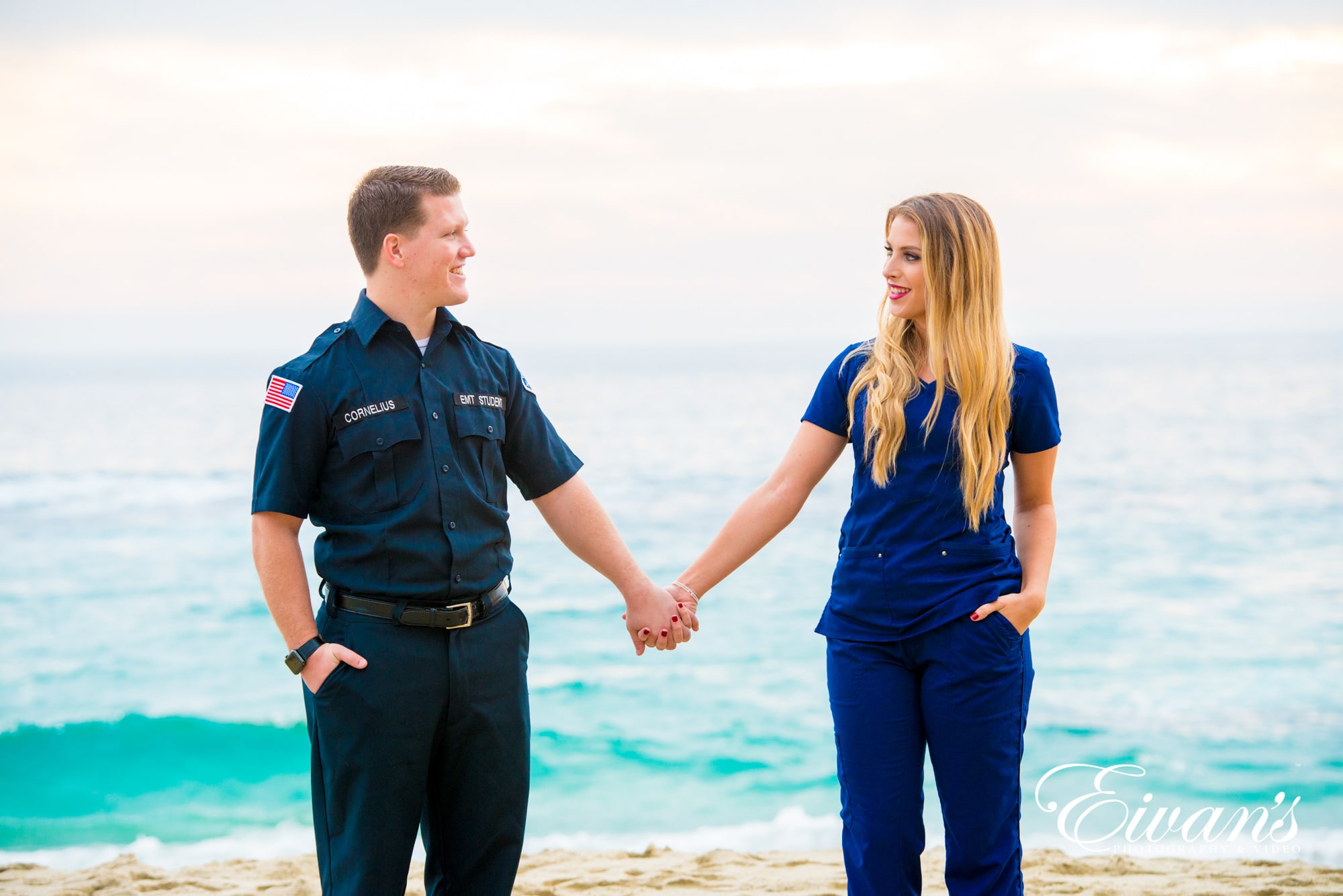 engaged couple holding hands in front of the water on a beach