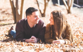 engaged couple posed on the ground surrounded by autumn leaves