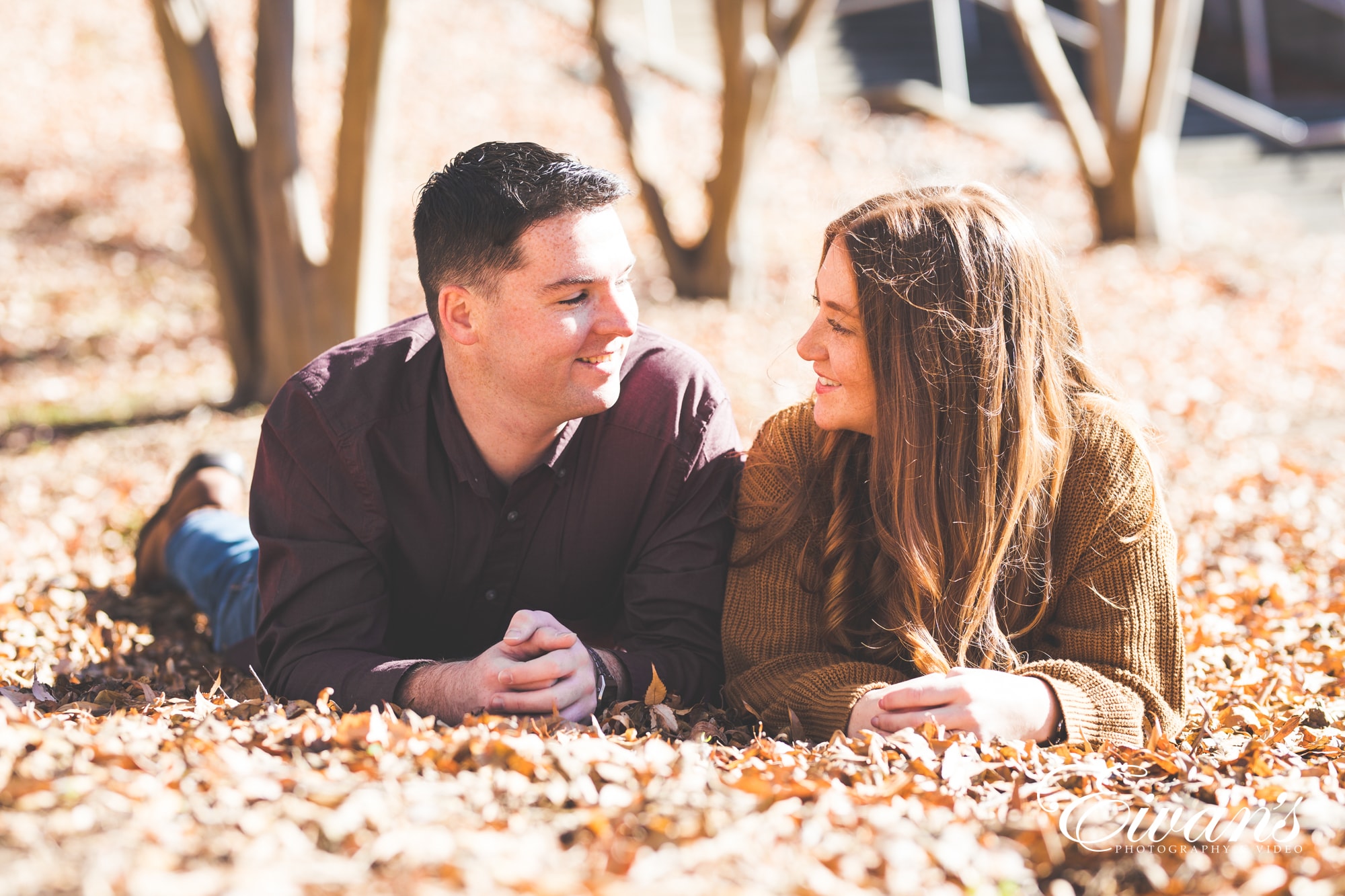 engaged couple posed on the ground surrounded by autumn leaves