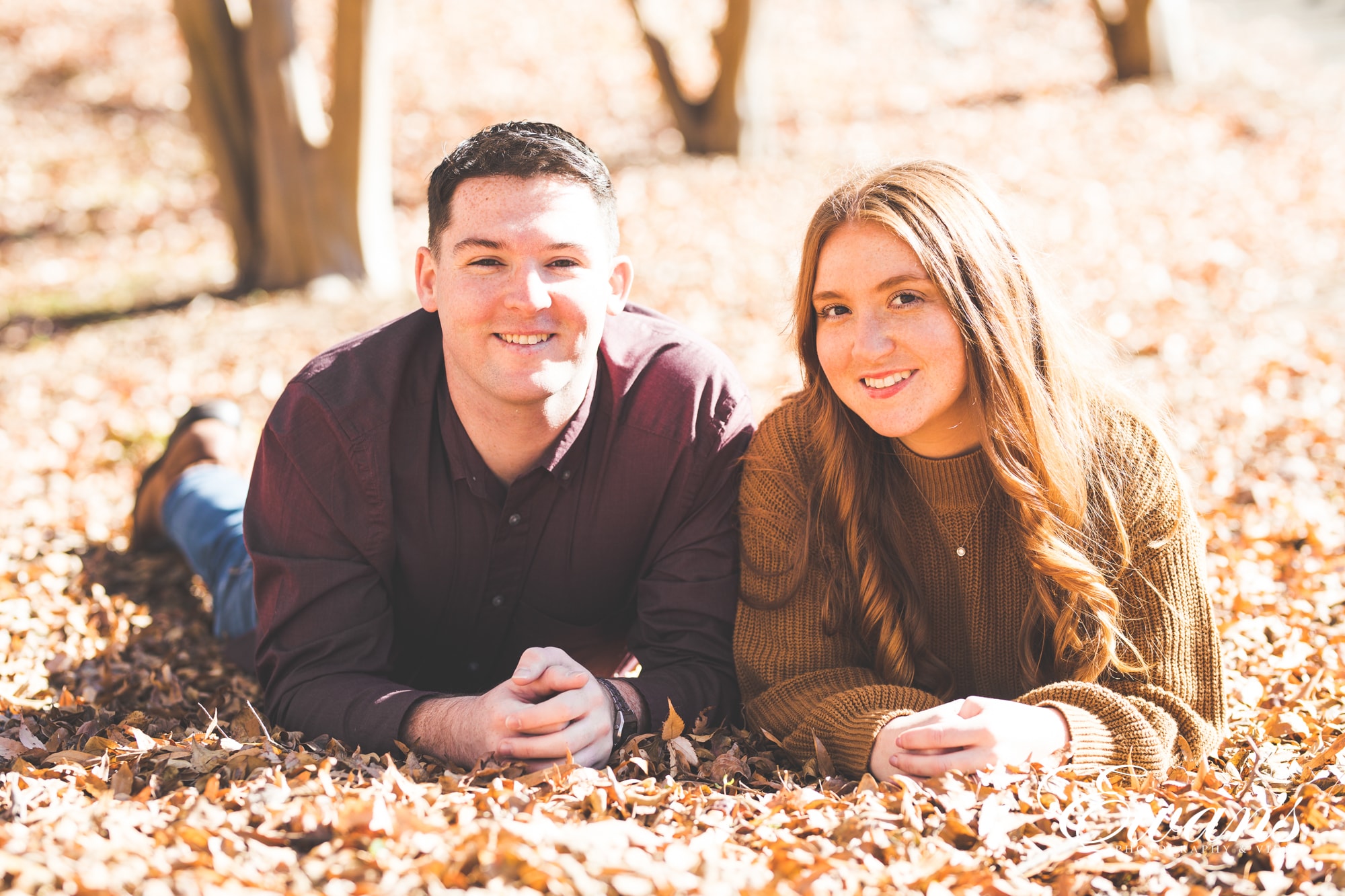 what-to-wear-for-your-engagement-photos-outdoors-complement-the-season couple posed on the group surrounded by autumn leaves