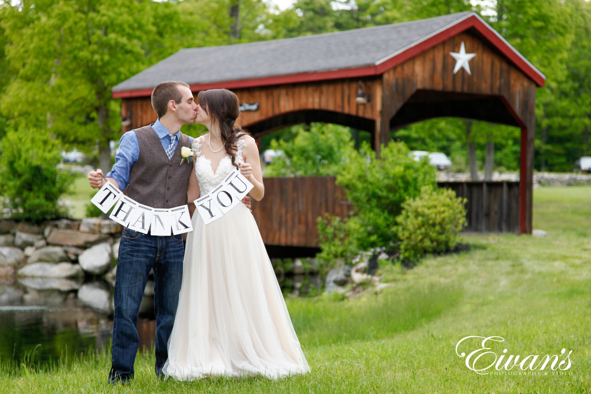 image of a bride and groom kissing while holding up a thank you sign