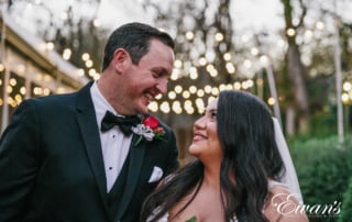 image of a bride and groom looking into each others eyes and smiling under fairy lights