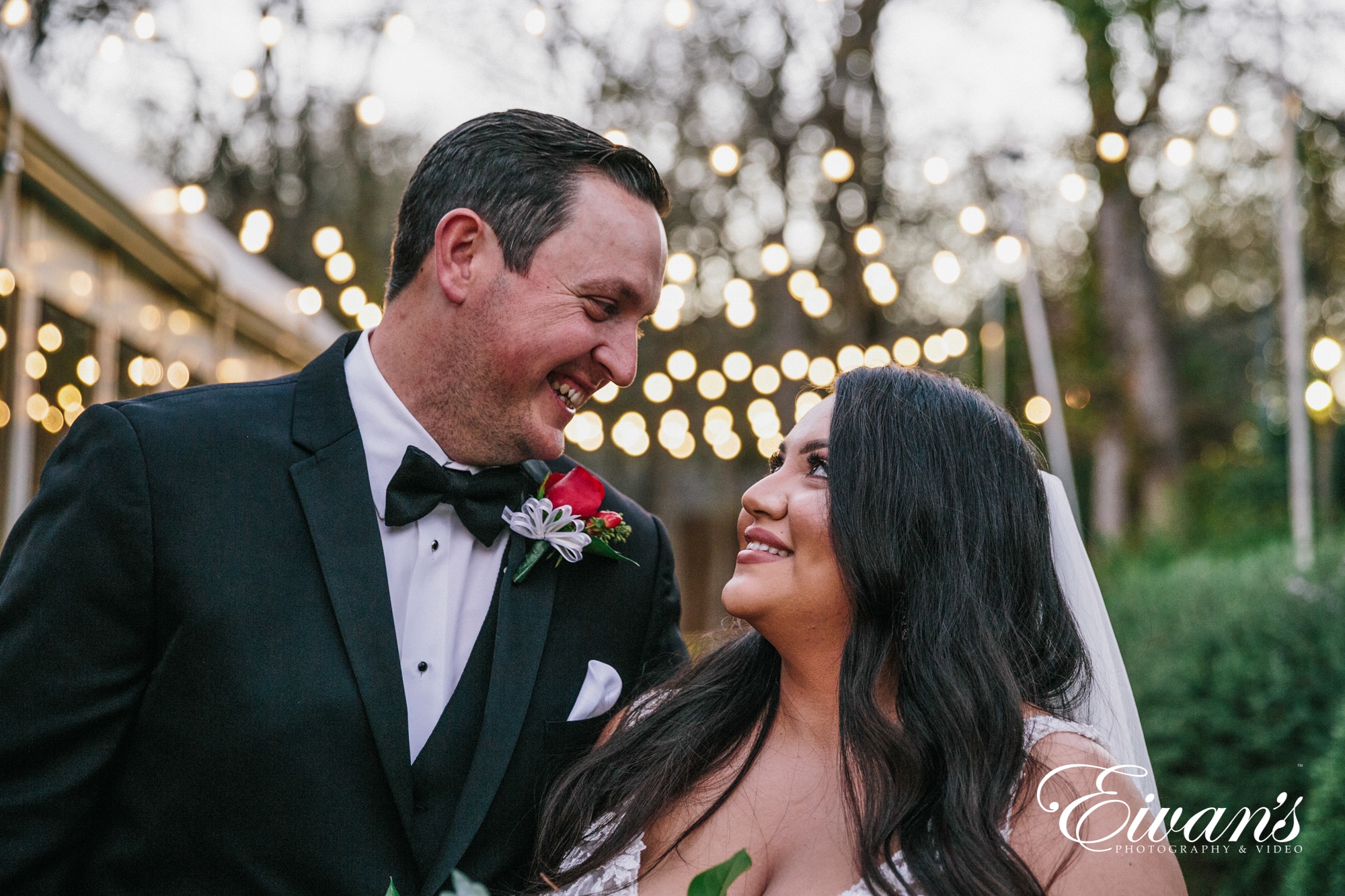 image of a bride and groom looking into each others eyes and smiling under fairy lights