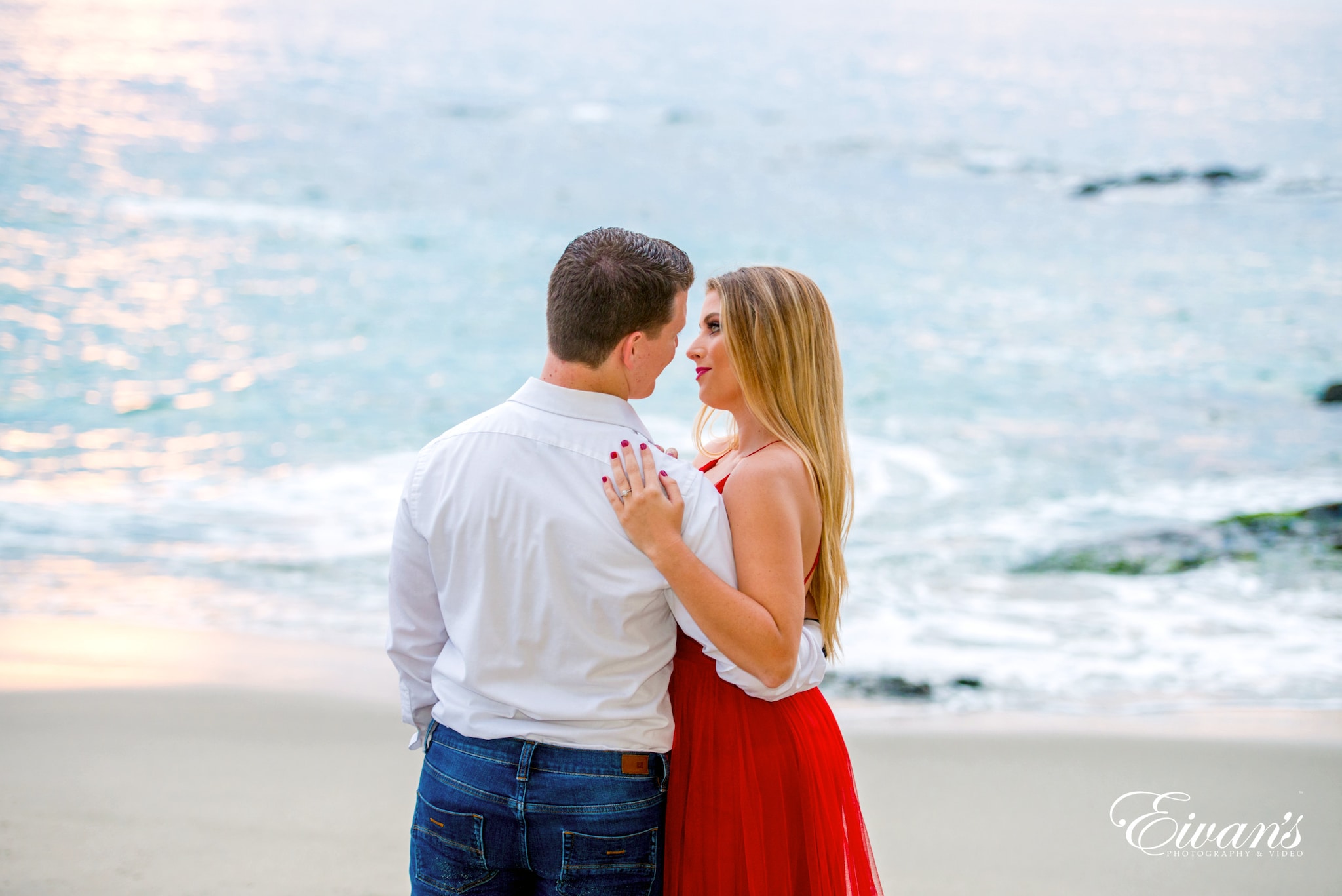 man in white shirt kissing woman in red dress on beach during daytime