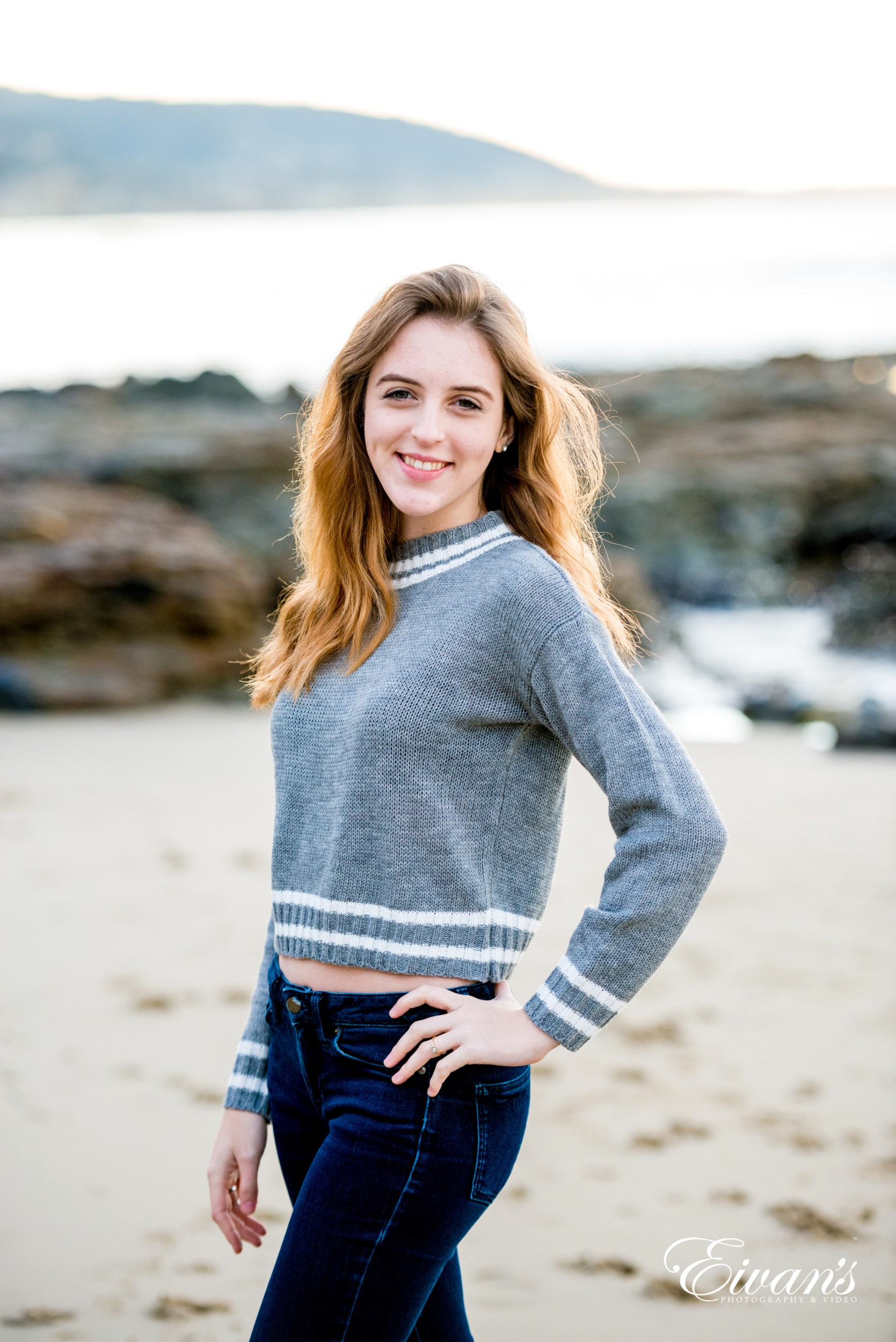 woman in gray long sleeve shirt and blue denim jeans standing on beach during daytime