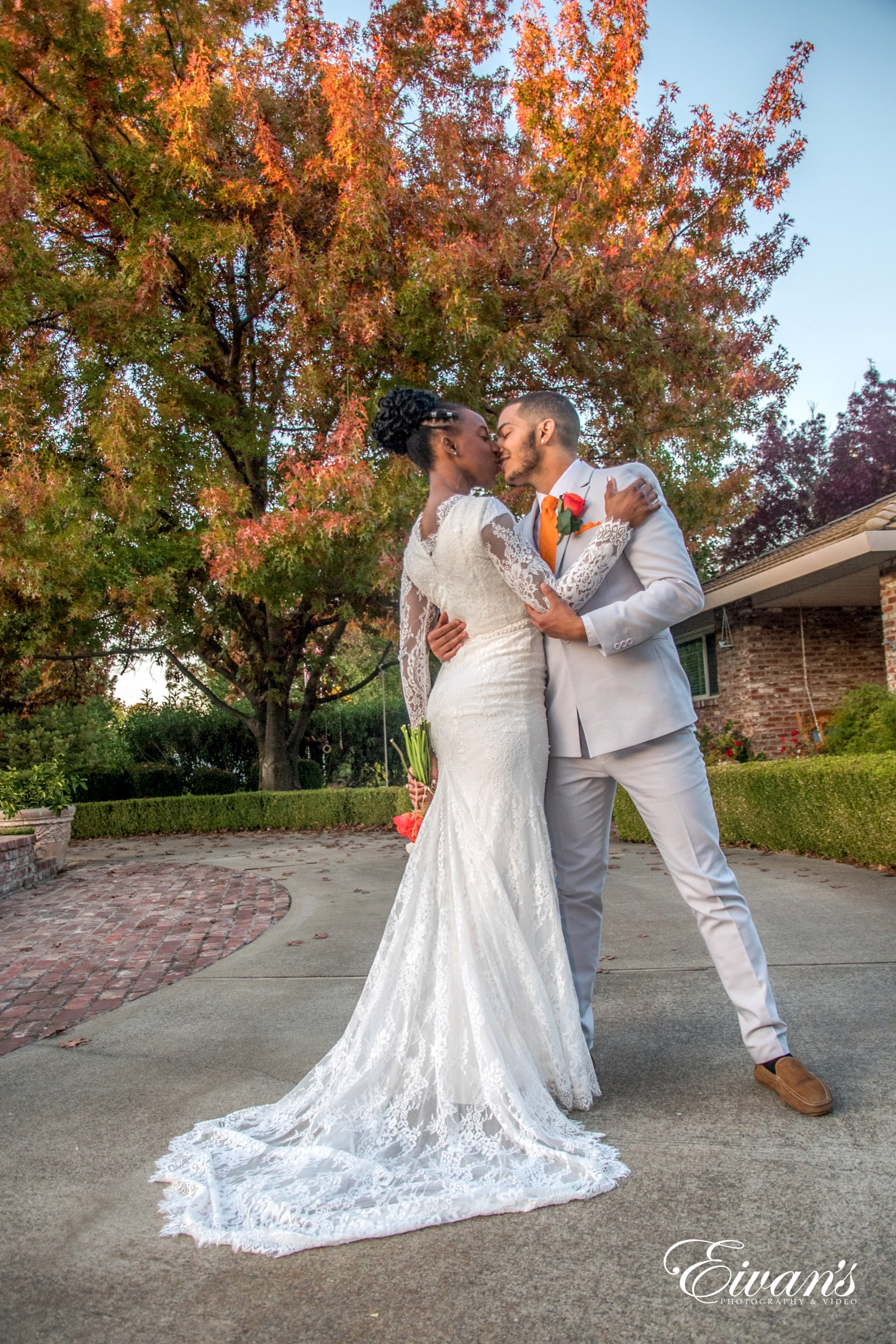 man in white suit kissing woman in white wedding dress on gray concrete pathway during daytime