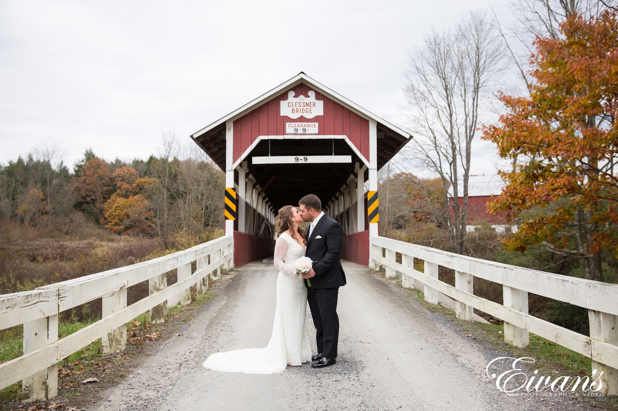 man in black suit kissing woman in white wedding dress on gray asphalt road during daytime