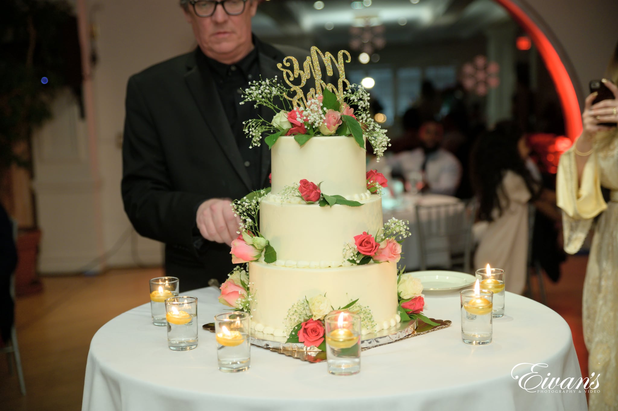 man in black suit jacket holding white and green floral cake