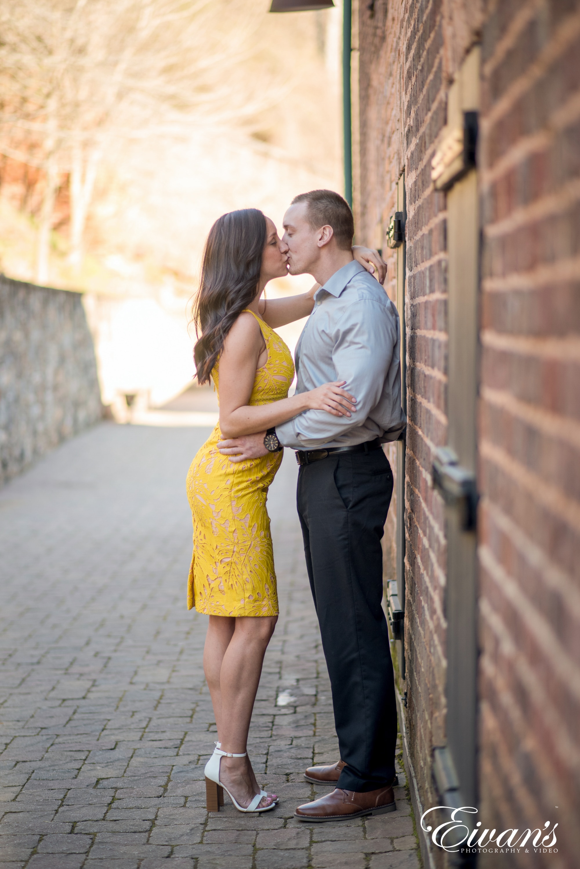 man and woman kissing beside brick wall during daytime