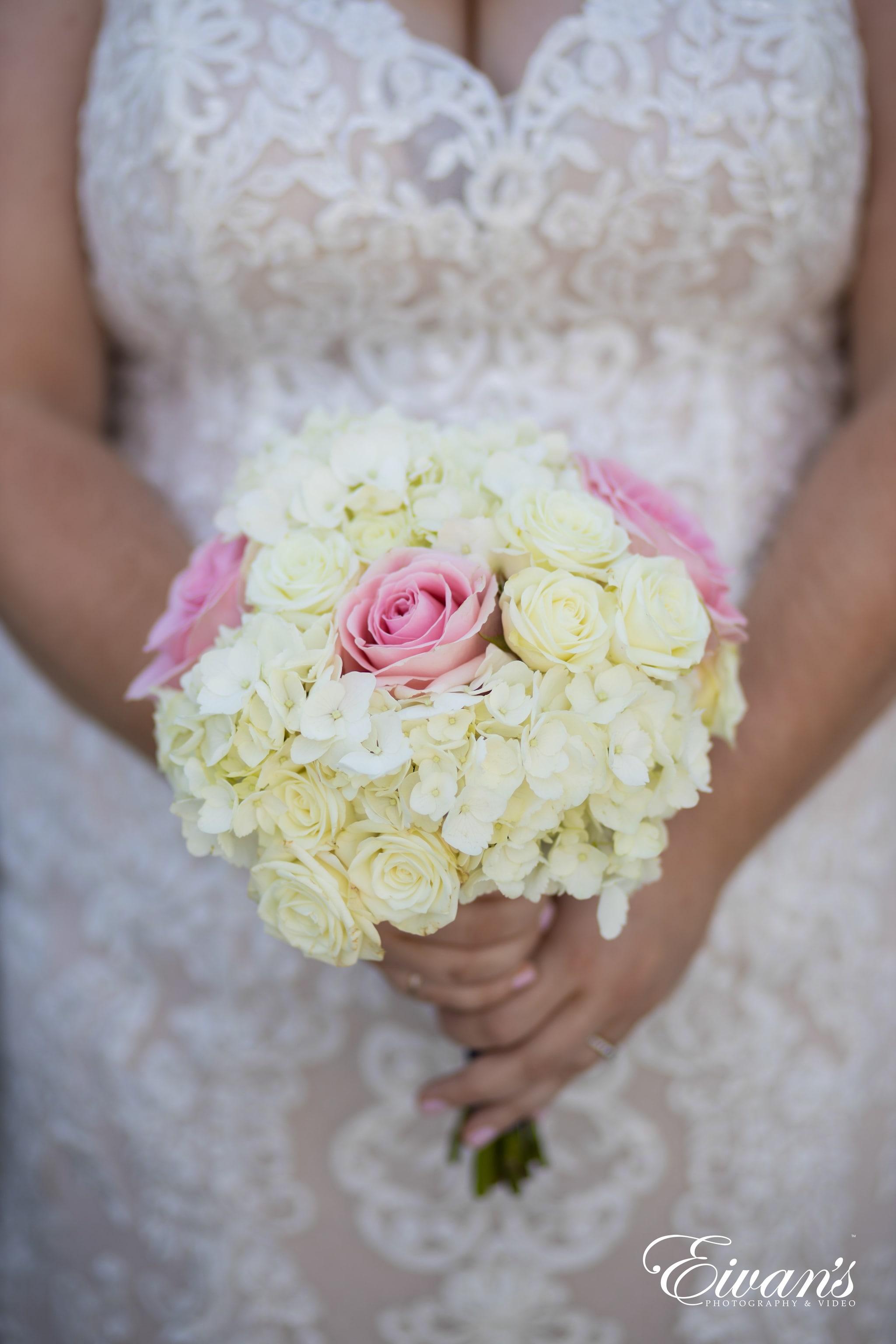 woman in white floral lace dress holding bouquet of white and pink roses
