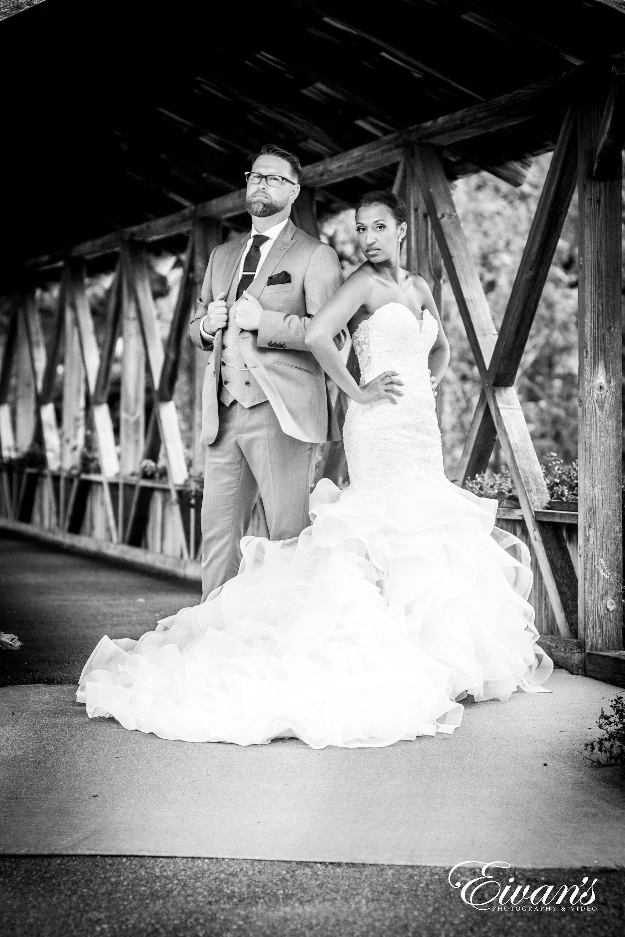 grayscale photo of bride and groom walking on wooden bridge