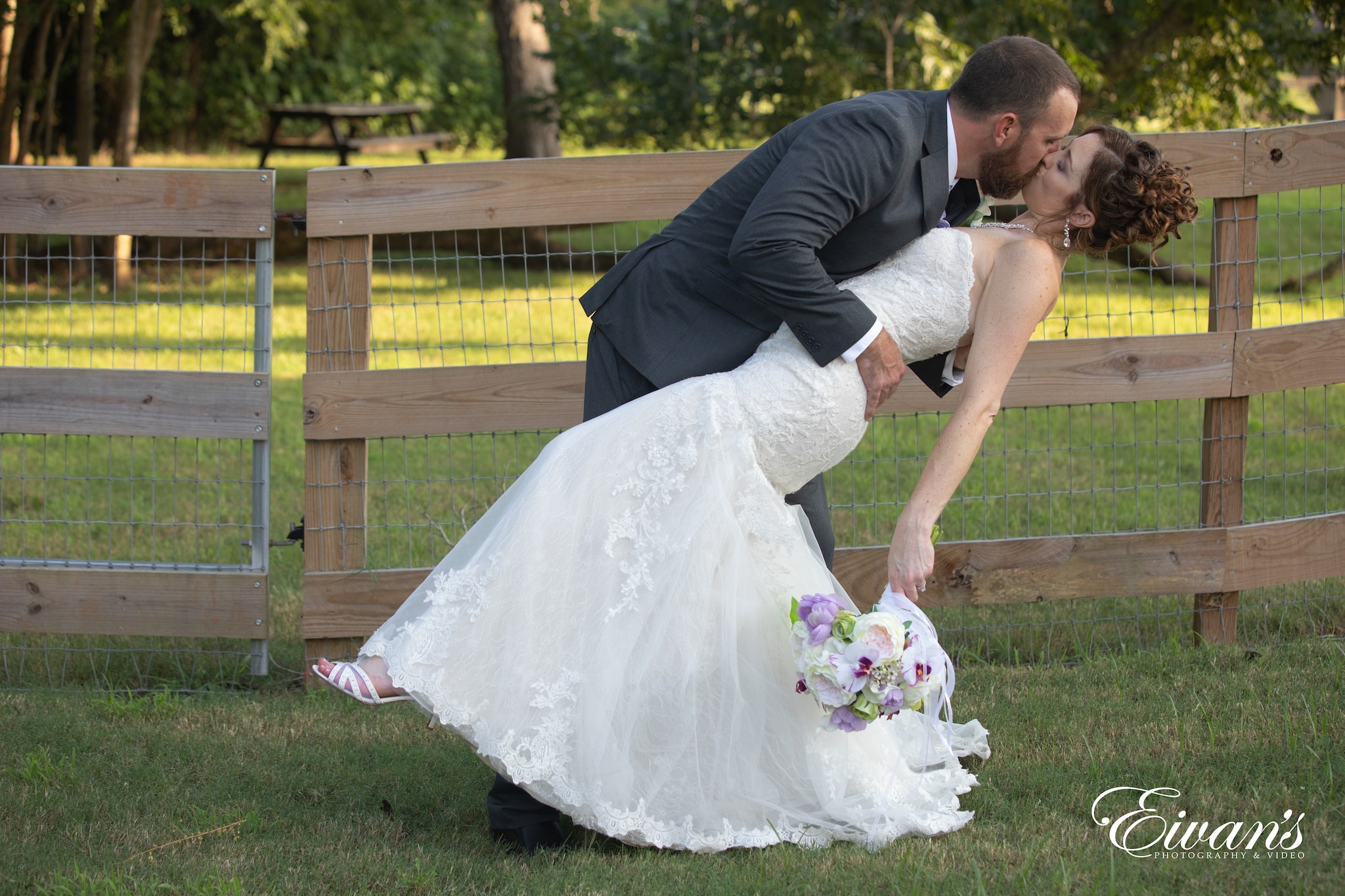 man in black suit kissing woman in white wedding dress on green grass field during daytime